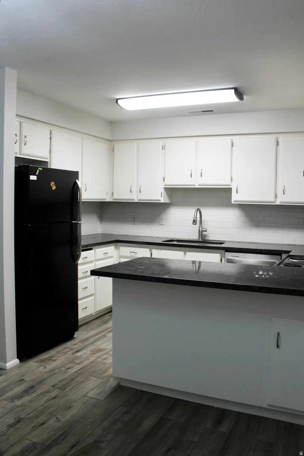 Kitchen featuring white cabinetry, dark countertops, a subway tile backsplash, a stainless steel sink with a gooseneck faucet, and wood-finish flooring