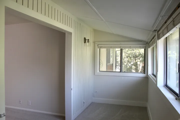 Carpeted room with multiple windows, an angled ceiling, and a wall-mounted light fixture