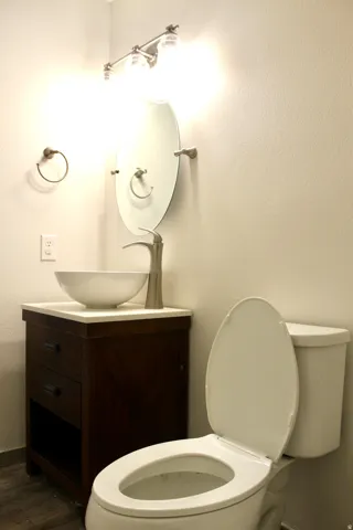 Vessel sink with a brushed nickel faucet, wood-finish vanity, white countertop, and wood-finish flooring