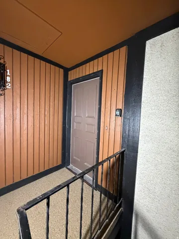 Entryway featuring vertical wood paneling, a panel door, black railings, and a granular textured floor