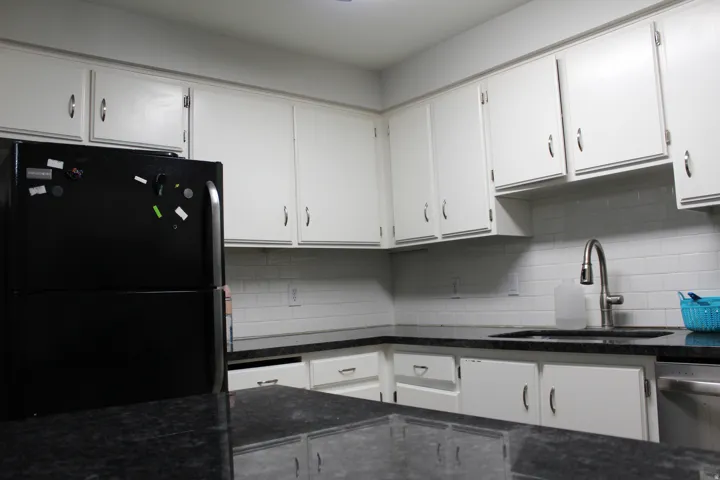 White shaker-style cabinetry, dark speckled countertops, subway tile backsplash, stainless steel kitchen sink, and a stainless steel pull-down faucet