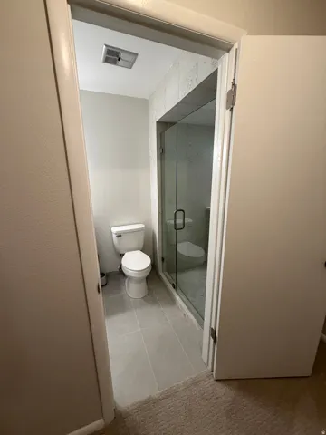 Modern bathroom featuring a sleek walk-in shower enclosure with frameless glass doors, ceramic tile flooring, recessed ceiling lighting, and a contemporary toilet fixture