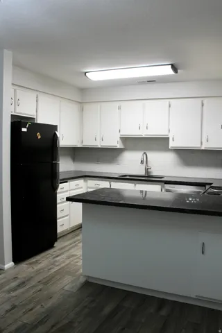 Kitchen featuring white cabinetry, dark countertops, a subway tile backsplash, a stainless steel sink with a gooseneck faucet, and wood-finish flooring