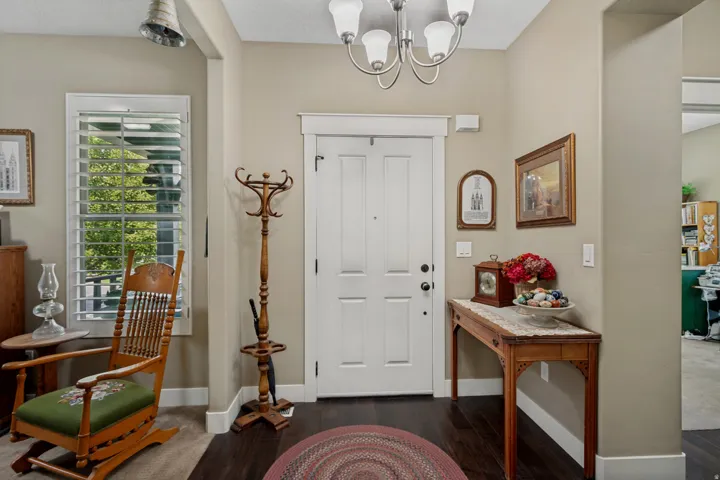 Front entry with dark wood-finish flooring, white paneled door, and white window shutters