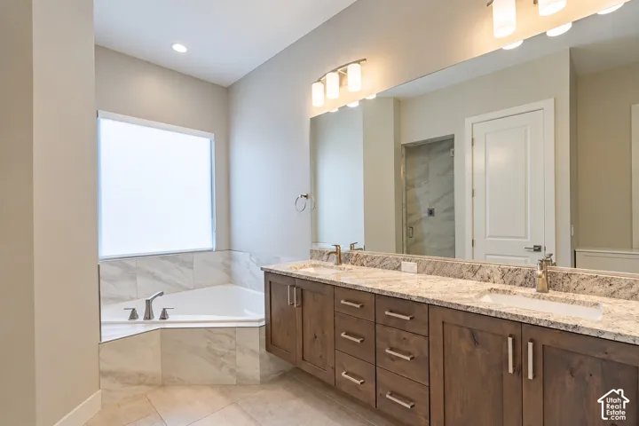 Dual vanity with stone countertop and integrated sinks, oversized mirror, built-in soaking tub with tile surround, and separate glass-enclosed shower