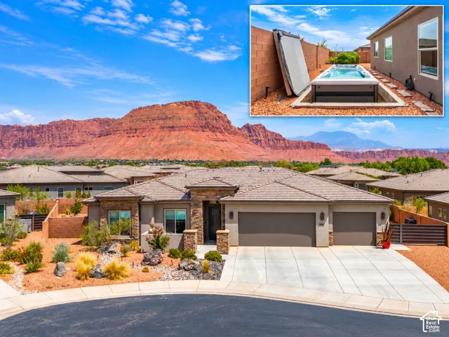 Exterior featuring a stone-accented facade, concrete driveway, three-car garage, red rock mountain backdrop, and a recessed swim spa with a masonry privacy wall
