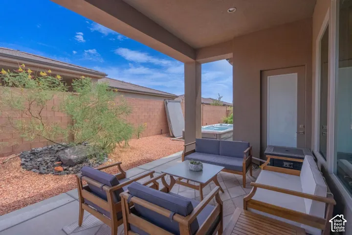 Covered patio featuring an outdoor spa, concrete slab, desert landscaping, and privacy wall