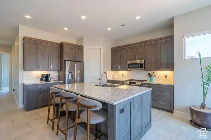 Large kitchen island with a stone countertop, recessed lighting, wood-finish cabinetry, stainless steel appliances, and tile flooring