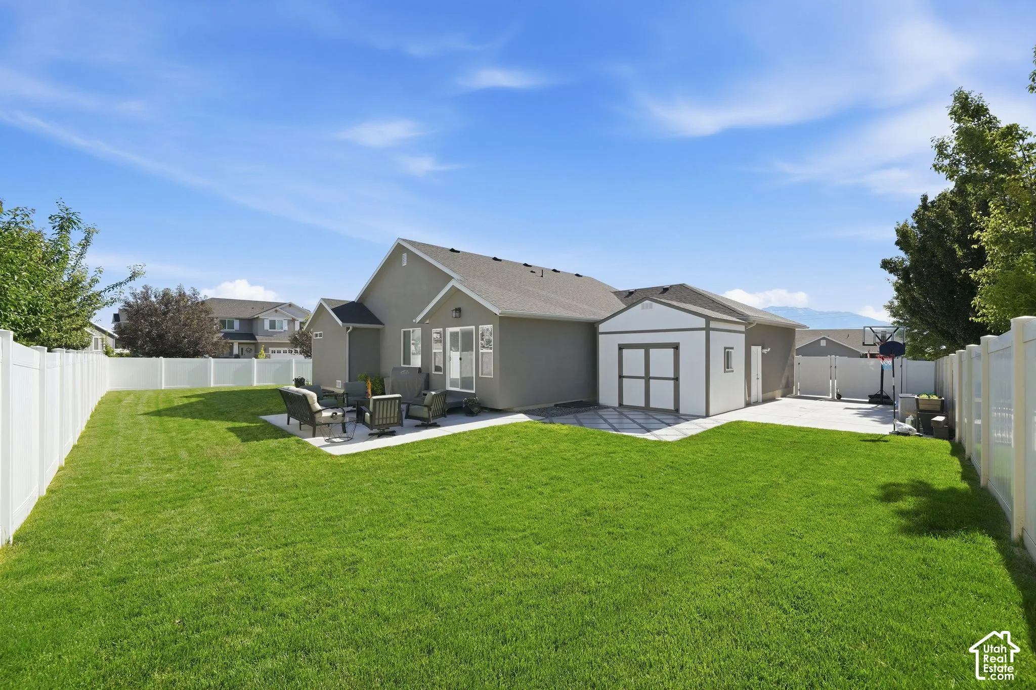 Expansive green lawn with a white vinyl privacy fence, concrete patio, and separate storage shed
