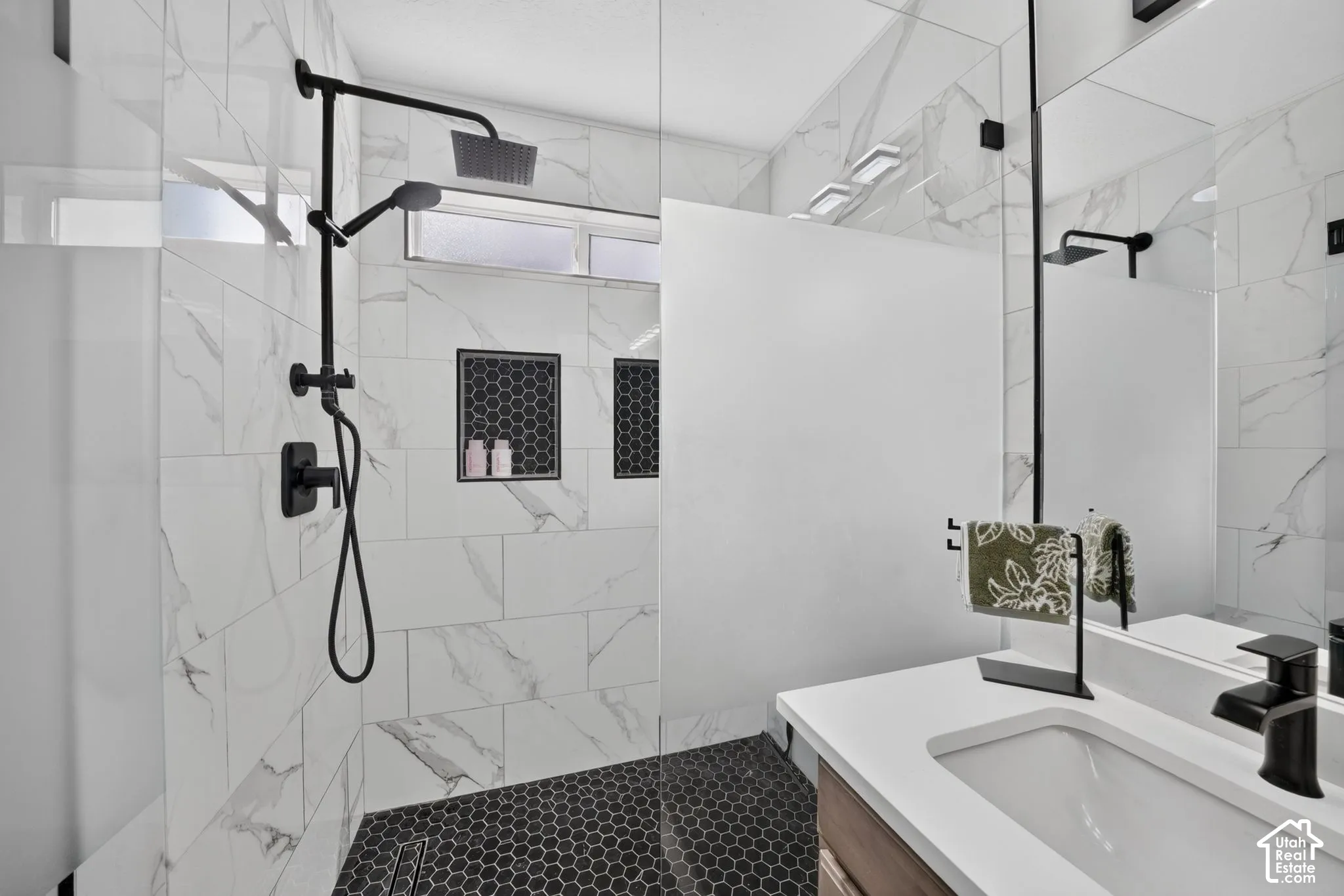 Shower with black hexagonal tile flooring, white marble-look wall tiling, and black-finish fixtures