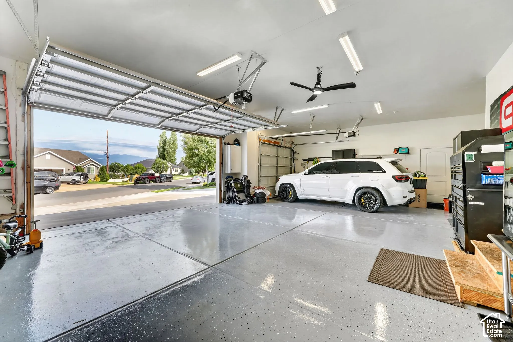 Attached two-car garage featuring a gray epoxy floor, ceiling fan, and fluorescent lighting fixtures