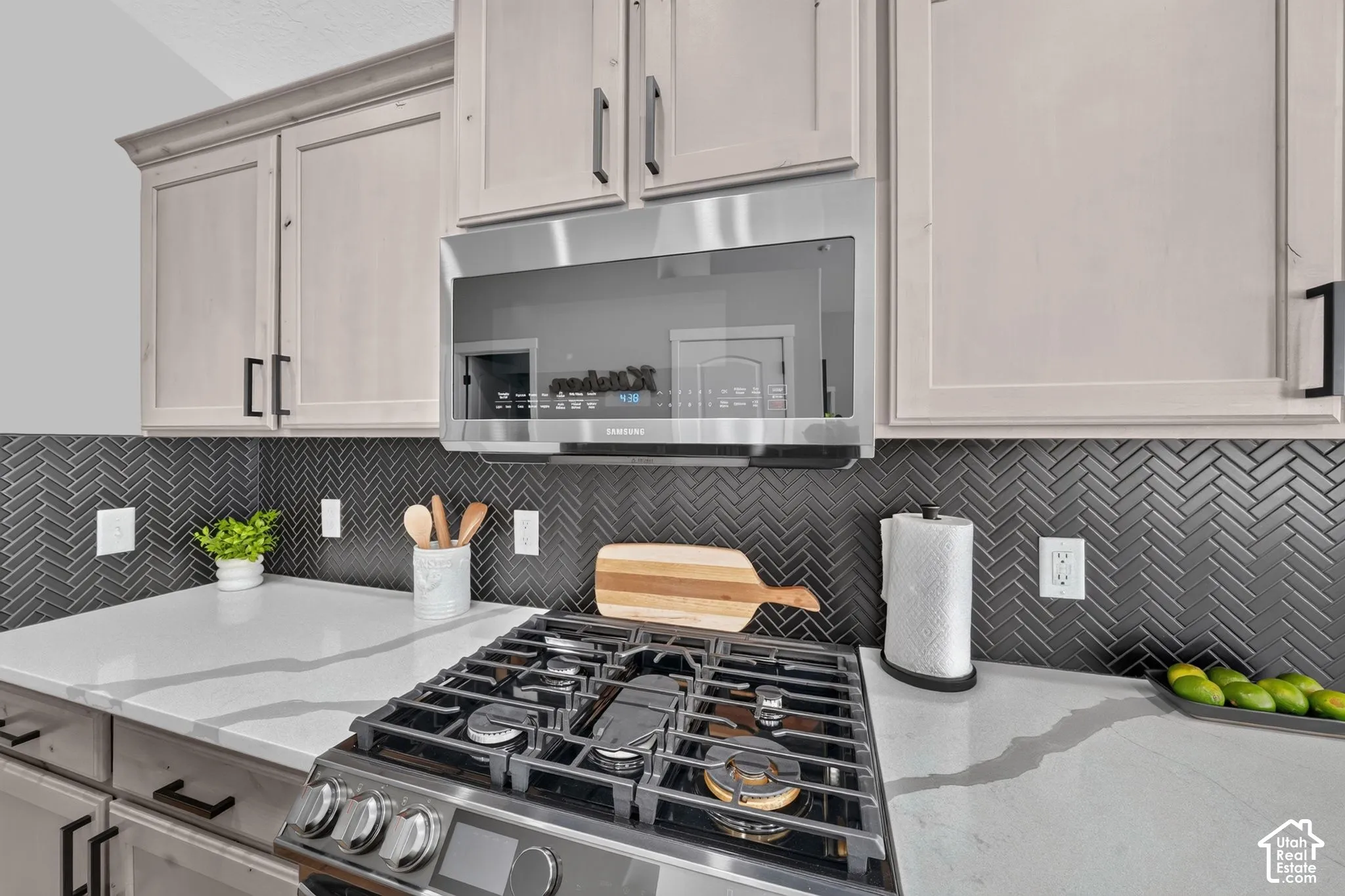 Stainless steel range, stainless steel microwave, light-toned cabinetry, dark herringbone tile backsplash, and light-toned countertops