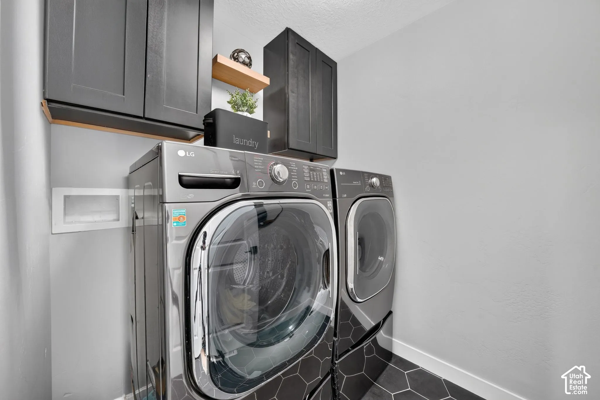Laundry area featuring dark cabinetry, a floating wood-tone shelf, and hexagonal floor tile