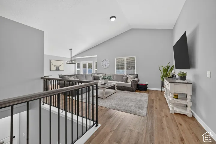Vaulted ceiling, wood-finish flooring, staircase with metal spindles, recessed lighting, and wall-mounted television