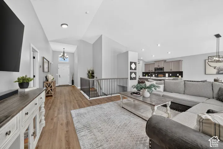 Vaulted ceilings, recessed lighting, wood-finish flooring, staircase with metal railing, and a kitchen with gray cabinetry