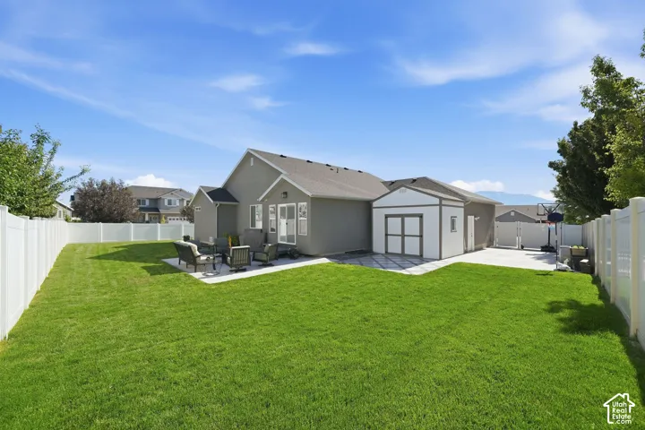 Expansive green lawn with a white vinyl privacy fence, concrete patio, and separate storage shed
