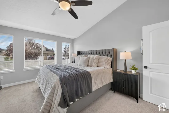 Vaulted ceiling, ceiling fan, multiple windows, carpet flooring, and a white interior door with dark hardware