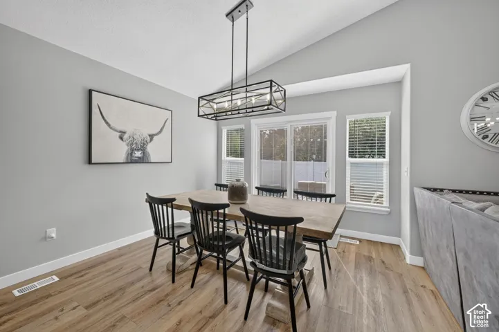 Vaulted ceiling, wood-finish flooring, sliding glass door, white trim, and a linear chandelier