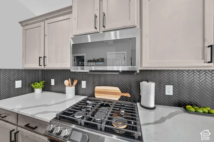 Stainless steel range, stainless steel microwave, light-toned cabinetry, dark herringbone tile backsplash, and light-toned countertops