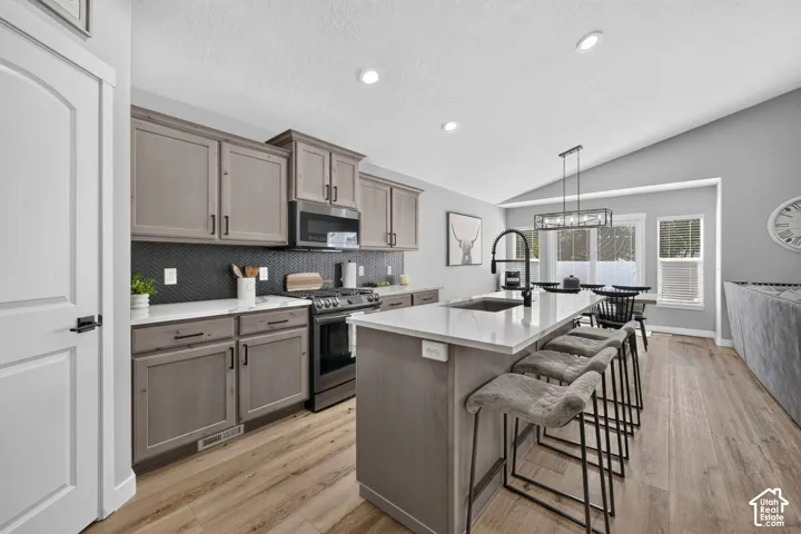 Vaulted ceiling kitchen featuring wood-finish flooring, recessed lighting, gray cabinetry with black hardware, and a white countertop island with an undermount sink