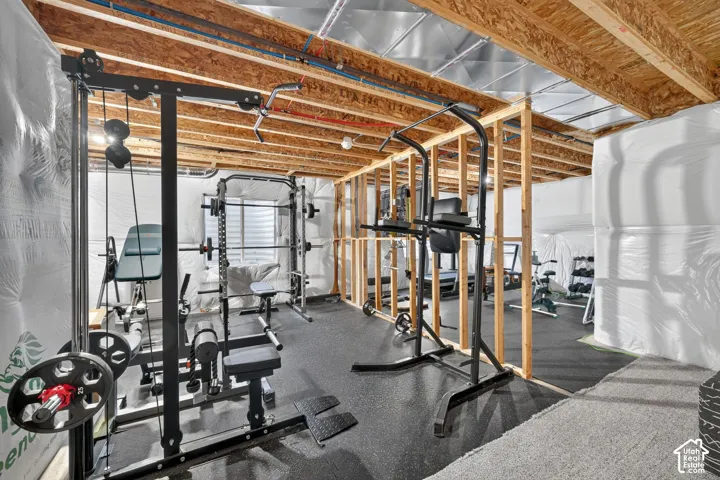 Unfinished basement with exposed ceiling joists and wood framing, featuring a rubber mat flooring section and a light-toned carpeted area