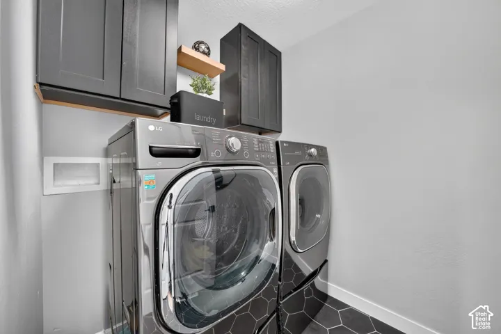 Laundry area featuring dark cabinetry, a floating wood-tone shelf, and hexagonal floor tile