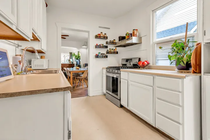 Bright galley kitchen featuring white cabinetry with shaker-style doors, wood-finish countertops, stainless steel gas range, and abundant natural light from multiple windows
