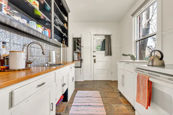 Wood-finish countertops, stainless steel sink with gooseneck faucet, white cabinetry, dark open shelving, and slate tile flooring