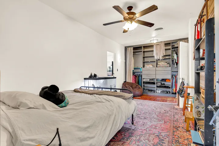 White walls with a ceiling fan, wood-finish flooring, and a built-in closet system