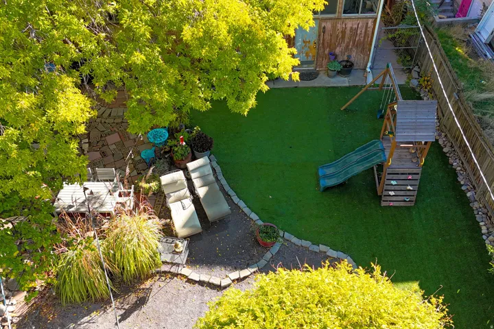 Expansive backyard featuring artificial turf, mature trees, and a stone patio area