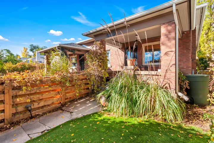 Brick exterior, covered porch, wood fence, manicured lawn, and lush landscaping