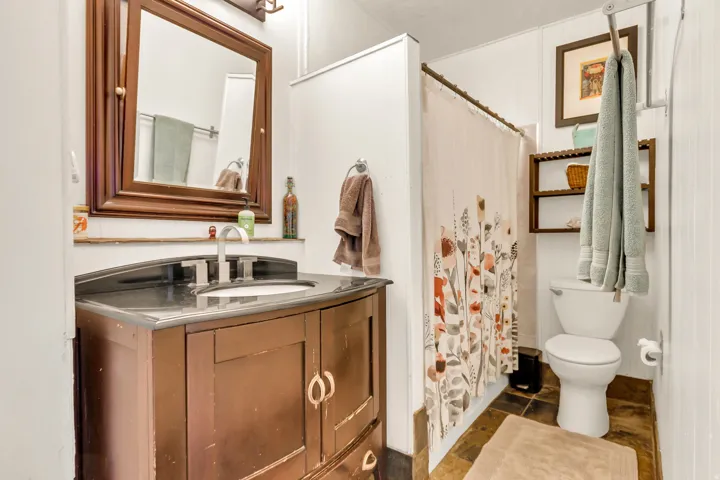 Vanity with a dark countertop and integrated sink, a rectangular framed mirror, tile flooring, and a shower area with a floral-patterned curtain