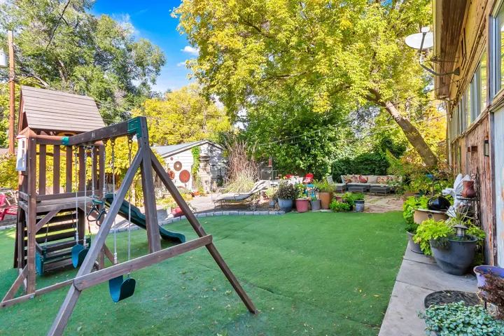 Expansive backyard featuring artificial turf, mature trees, a wooden play structure, and a patio area