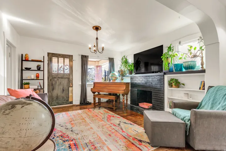Hardwood flooring, fireplace with a black brick surround, built-in shelving, white walls, and a multi-pane front door