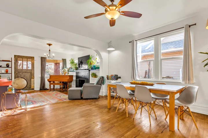 Hardwood flooring throughout, arched doorways, a built-in fireplace with a dark surround, and a ceiling fan with integrated lighting