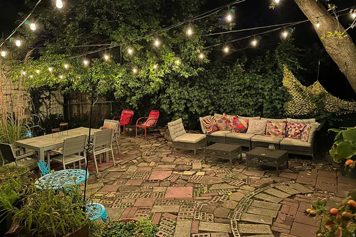 Brick paver patio with string lighting and established perimeter foliage