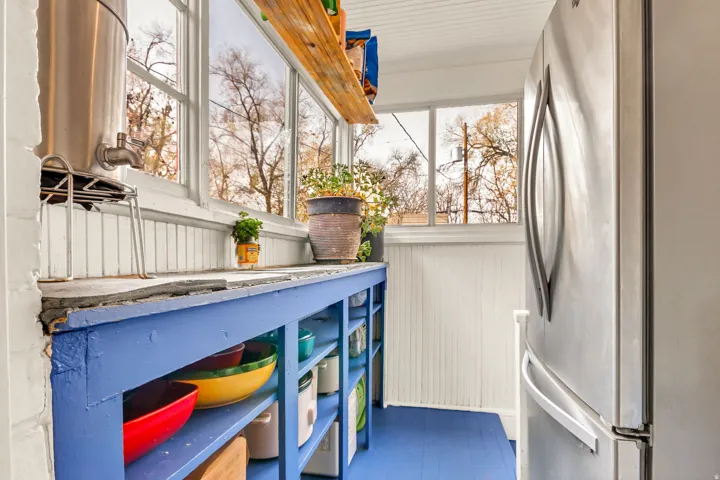 Stainless steel refrigerator, built-in shelving, expansive windows, beadboard wall paneling, and painted wood flooring