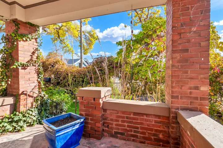 Brick porch columns with ivy accents, stone-capped brick pony walls, and dark metal railing