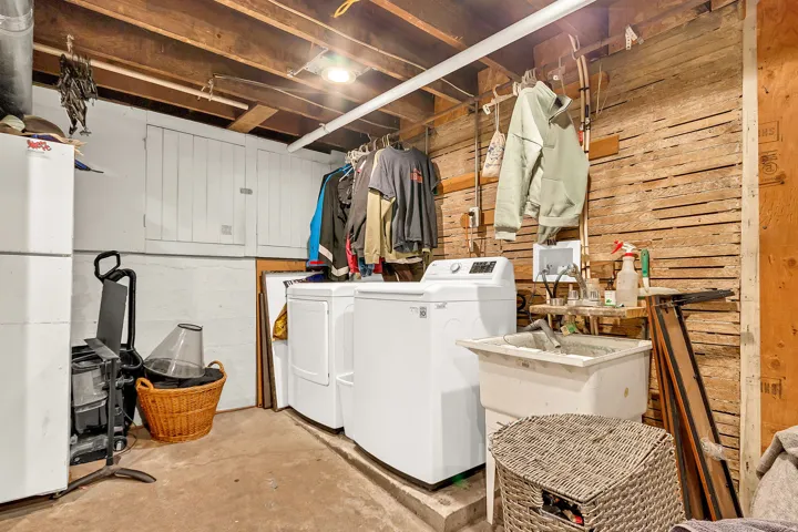 Laundry area with exposed wood ceiling joists, white concrete block walls, and a utility sink