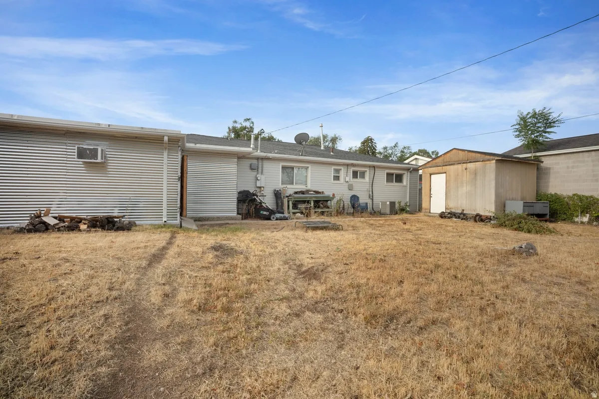 Expansive yard featuring a corrugated metal outbuilding with a window air conditioning unit, additional storage shed, and a main structure with a light-colored siding exterior