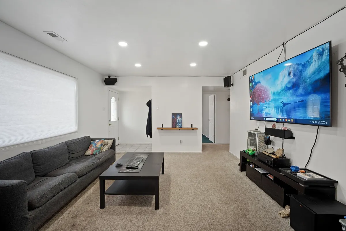 Carpeted living space featuring recessed lighting, a white door with a window, and a wall-mounted entertainment shelf