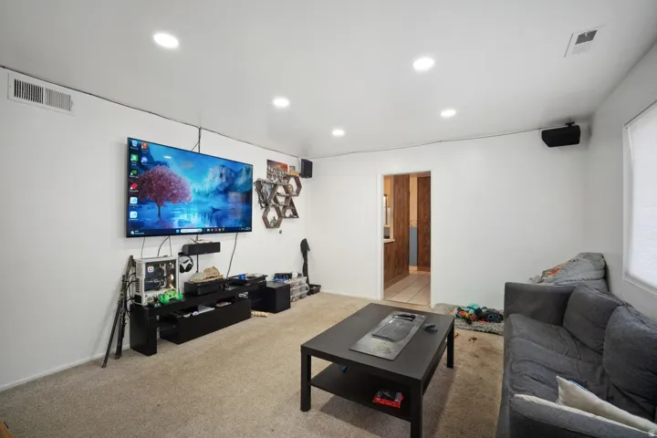 Recessed ceiling lighting, wall-mounted speakers, and a doorway with wood-finish flooring