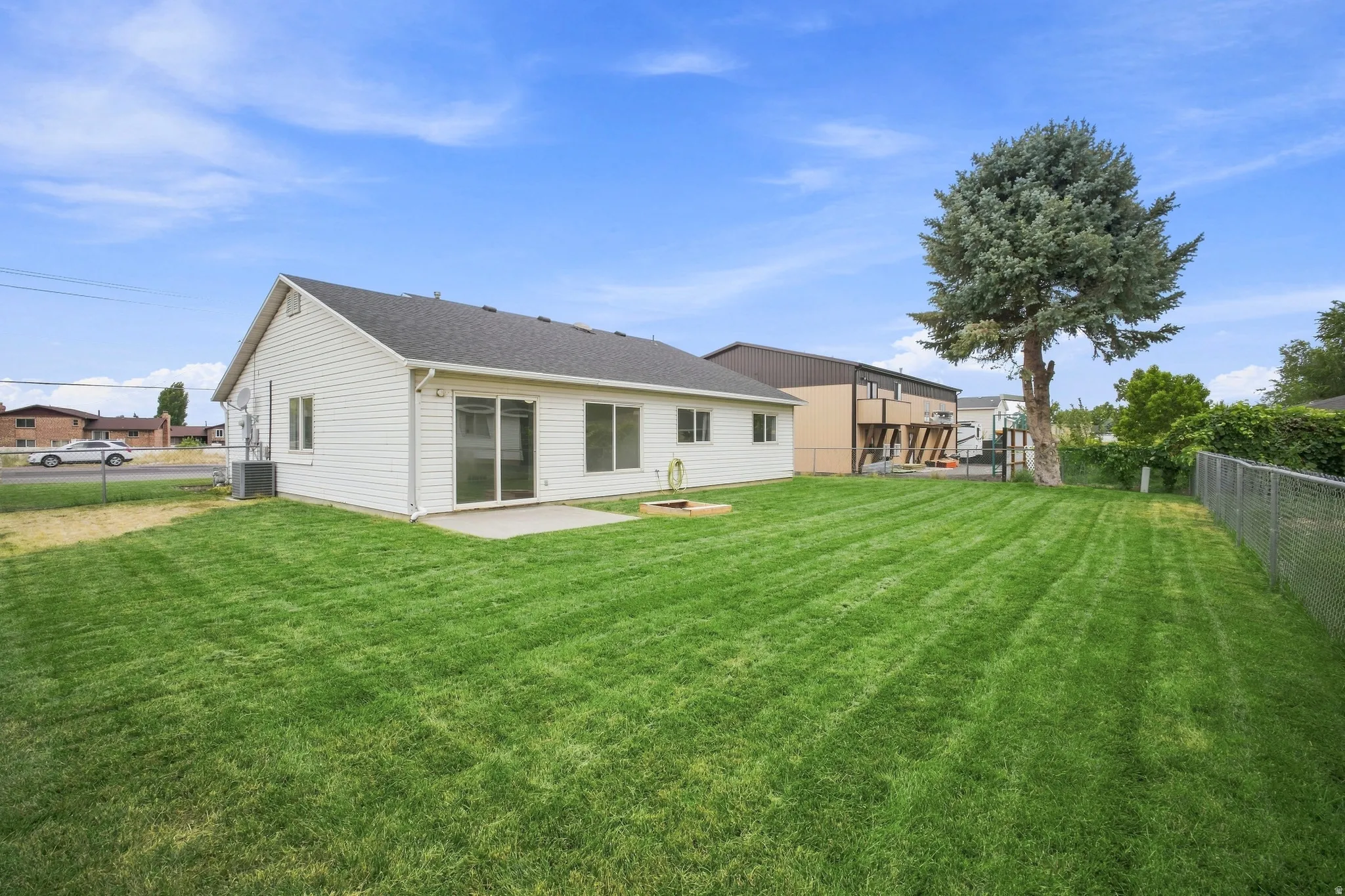 Expansive backyard with a large grass lawn, chain link fence, and a mature tree