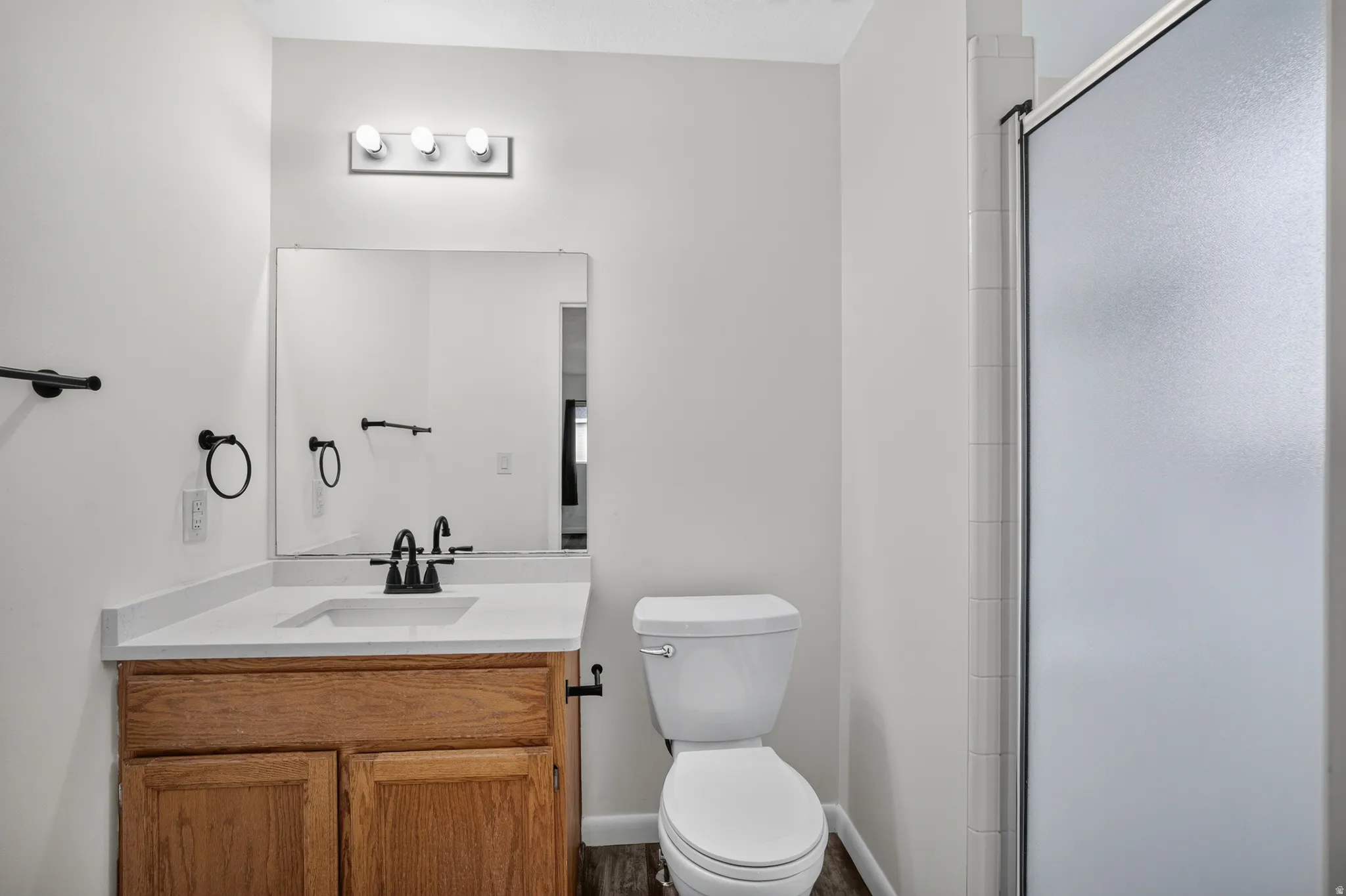 Bathroom featuring a wood-finish vanity with an integrated sink and white countertop, black fixtures, and a shower with a frosted glass enclosure