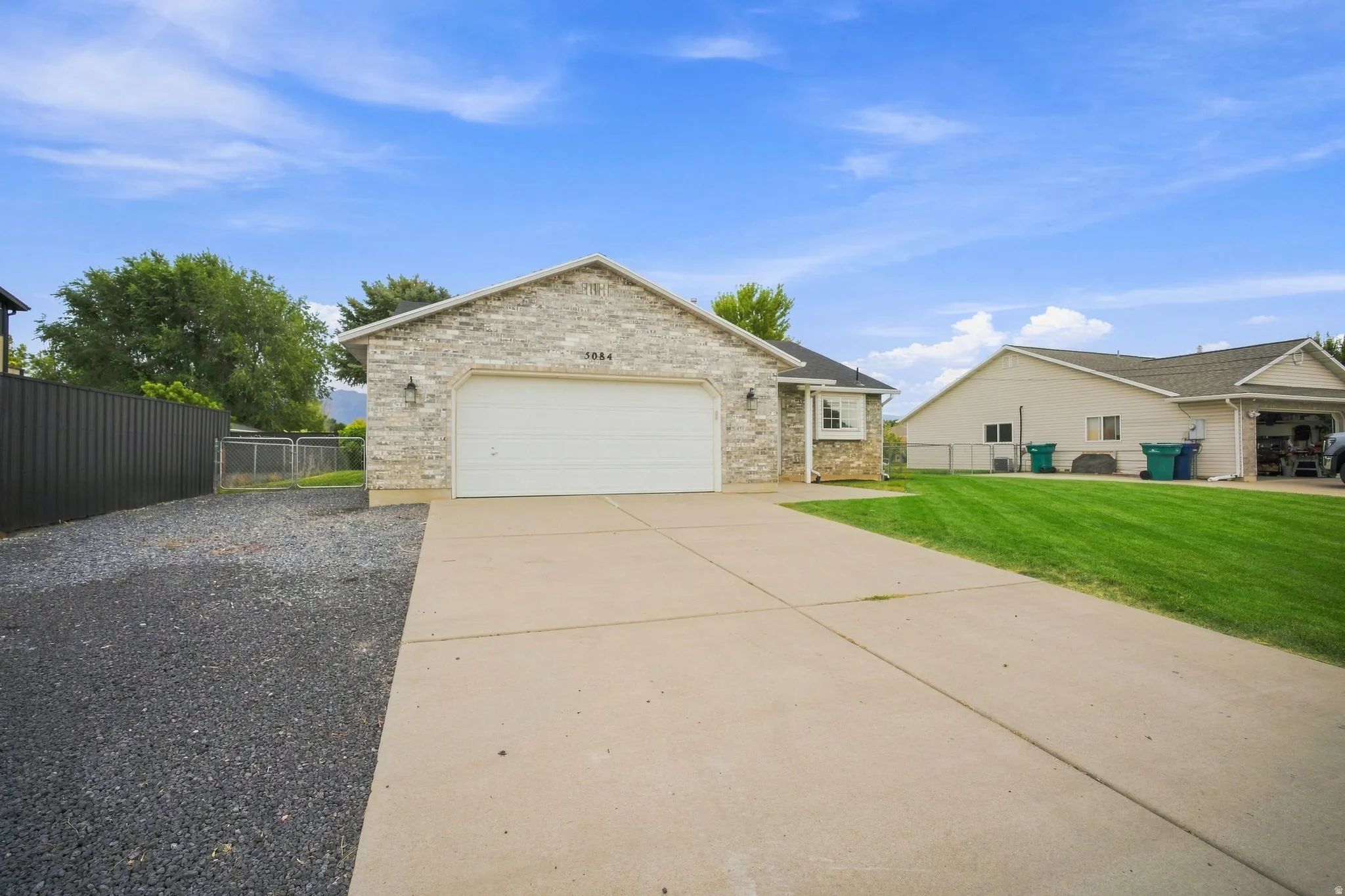 Stone veneer facade with an attached garage, concrete driveway, and a gravel side yard