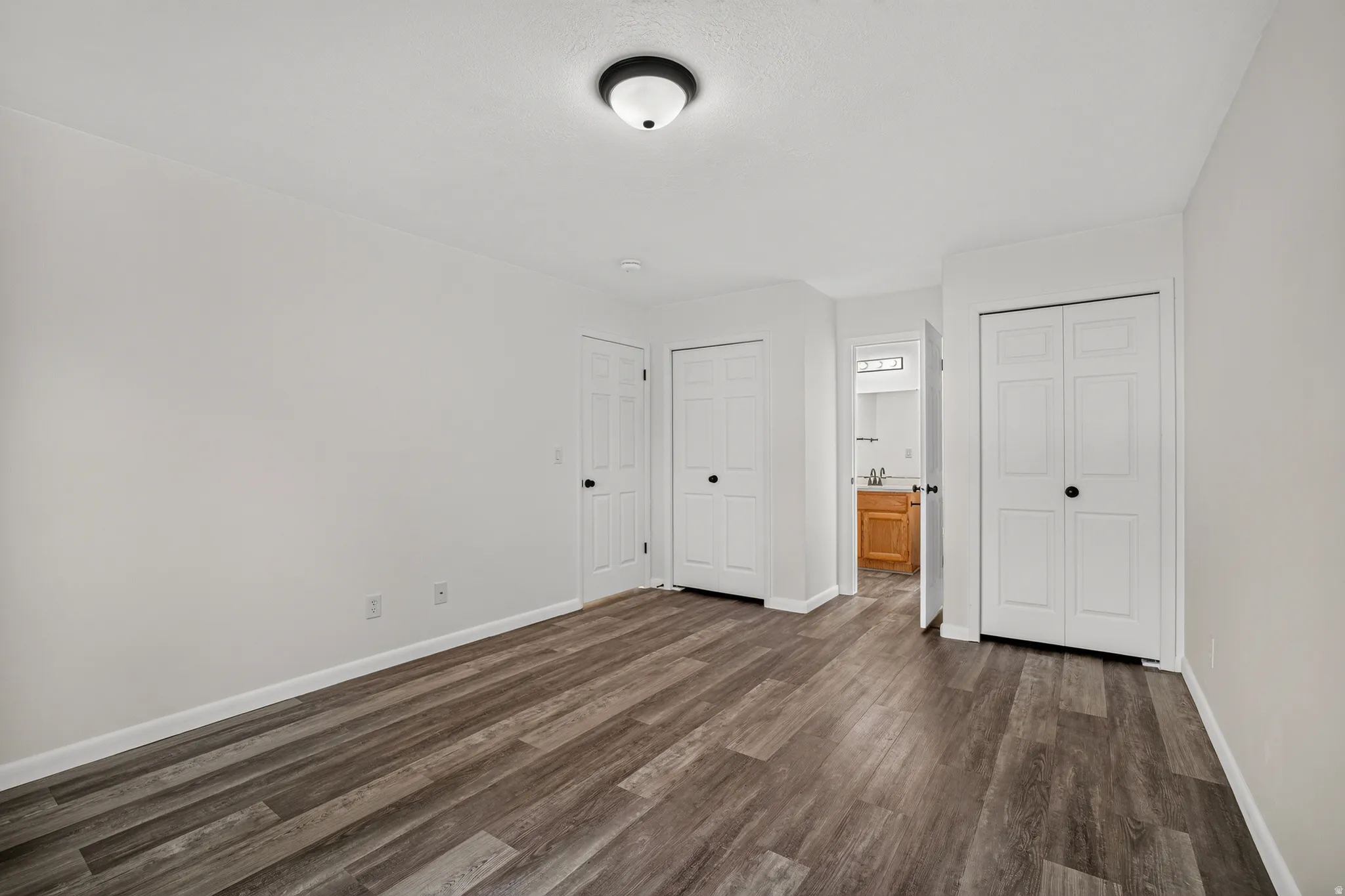 Wood-finish flooring, white painted walls, and ceiling-mounted light fixture