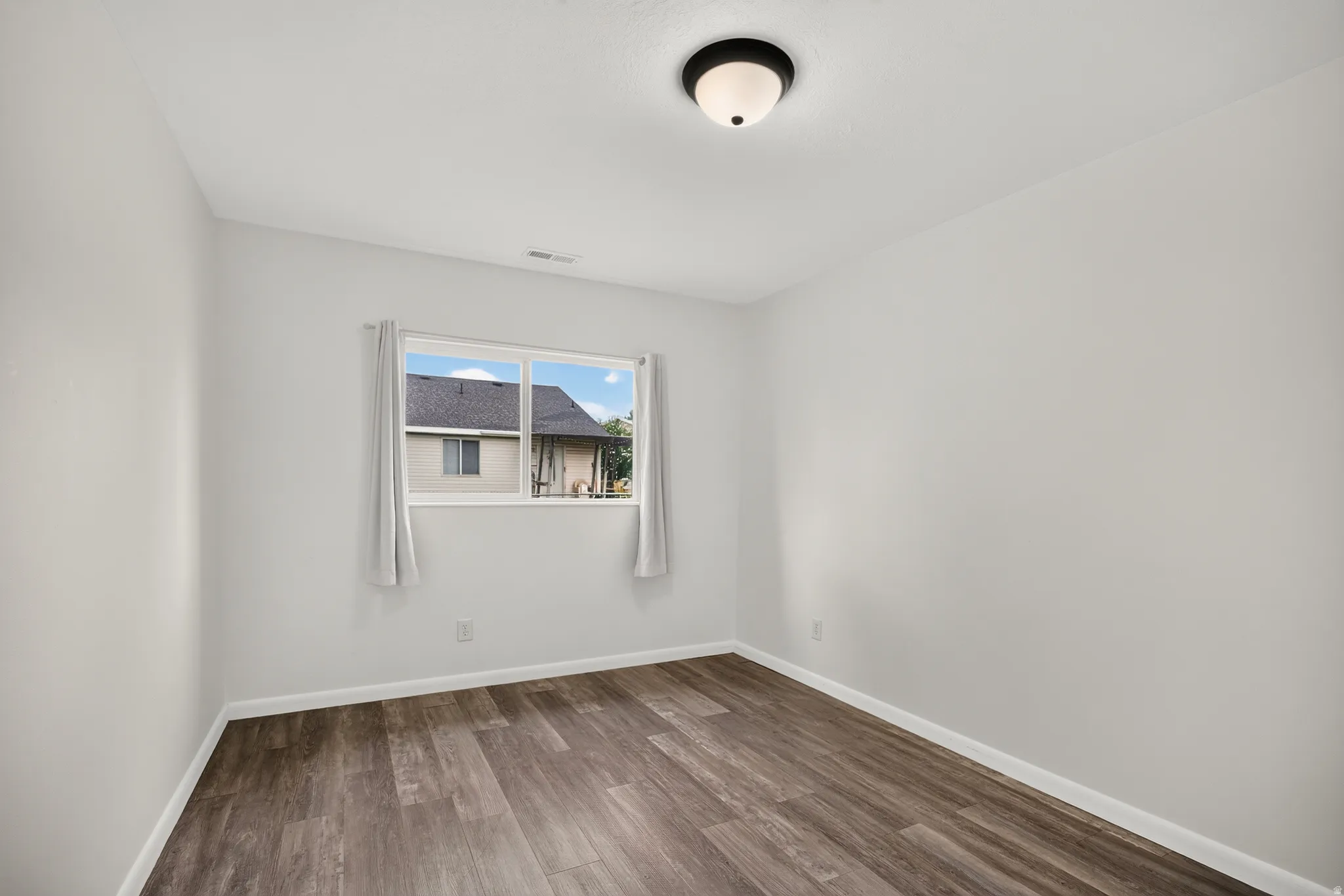 Wood-finish flooring with white baseboards, a flush-mount ceiling light fixture, and a window with white trim