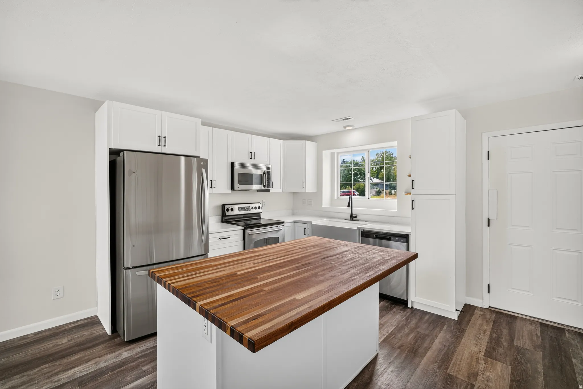 Kitchen featuring white cabinetry, stainless steel appliances, a butcher block island, and wood-finish flooring