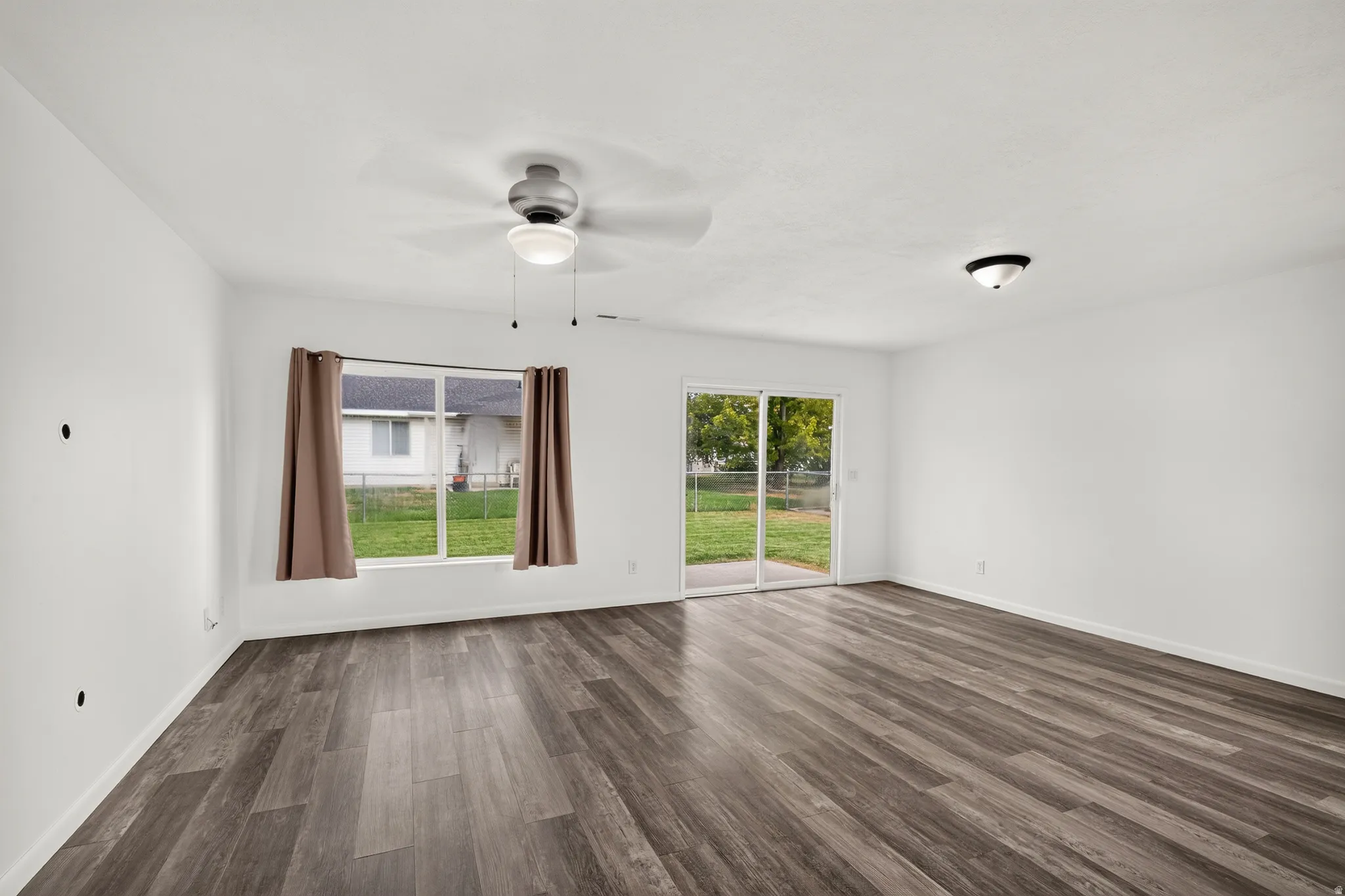 Spacious room featuring wood-finish flooring, white walls, and a ceiling fan with integrated lighting