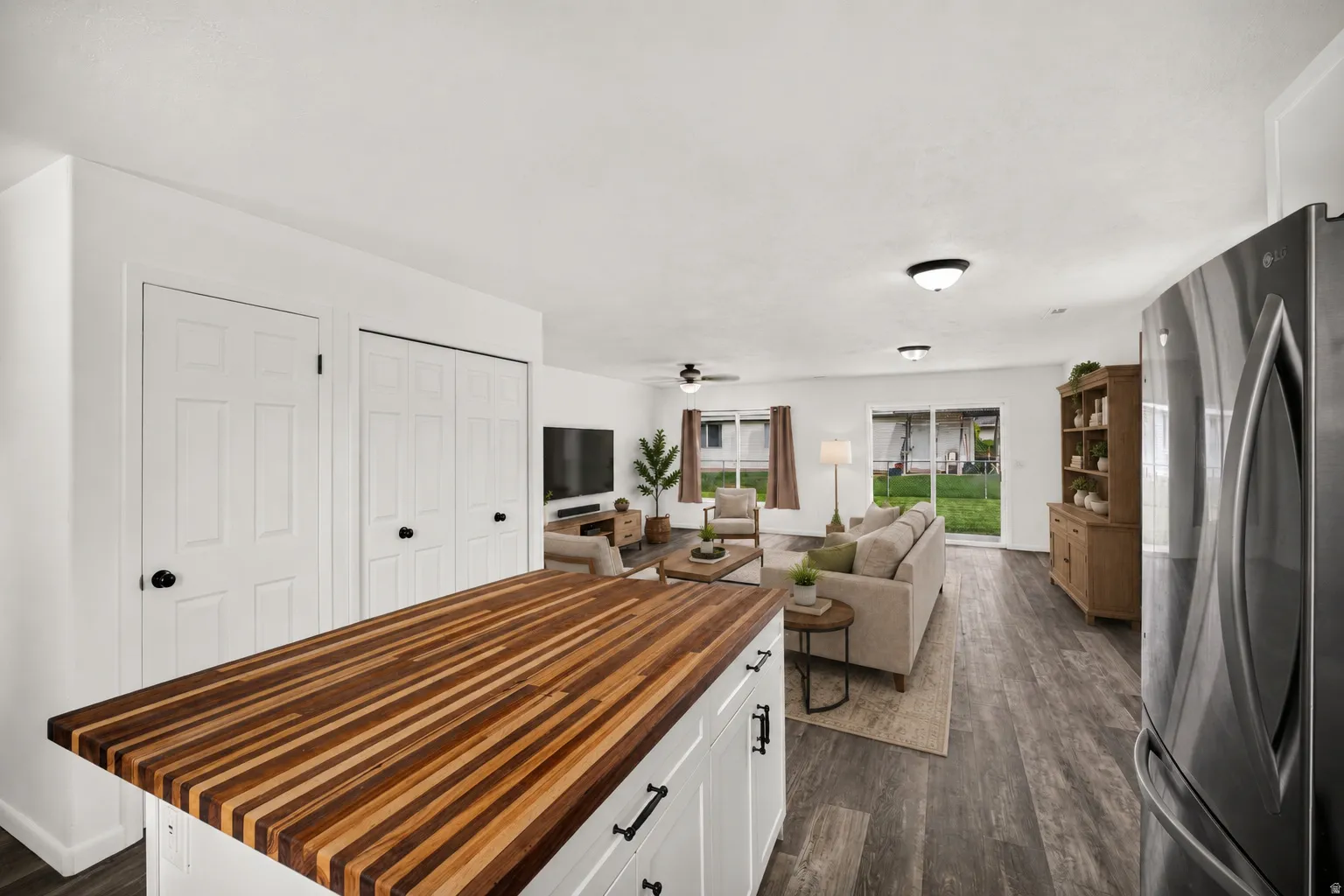 Virtually Staged - Butcher block countertop, white cabinetry, stainless steel refrigerator, wood-finish flooring, and sliding glass doors